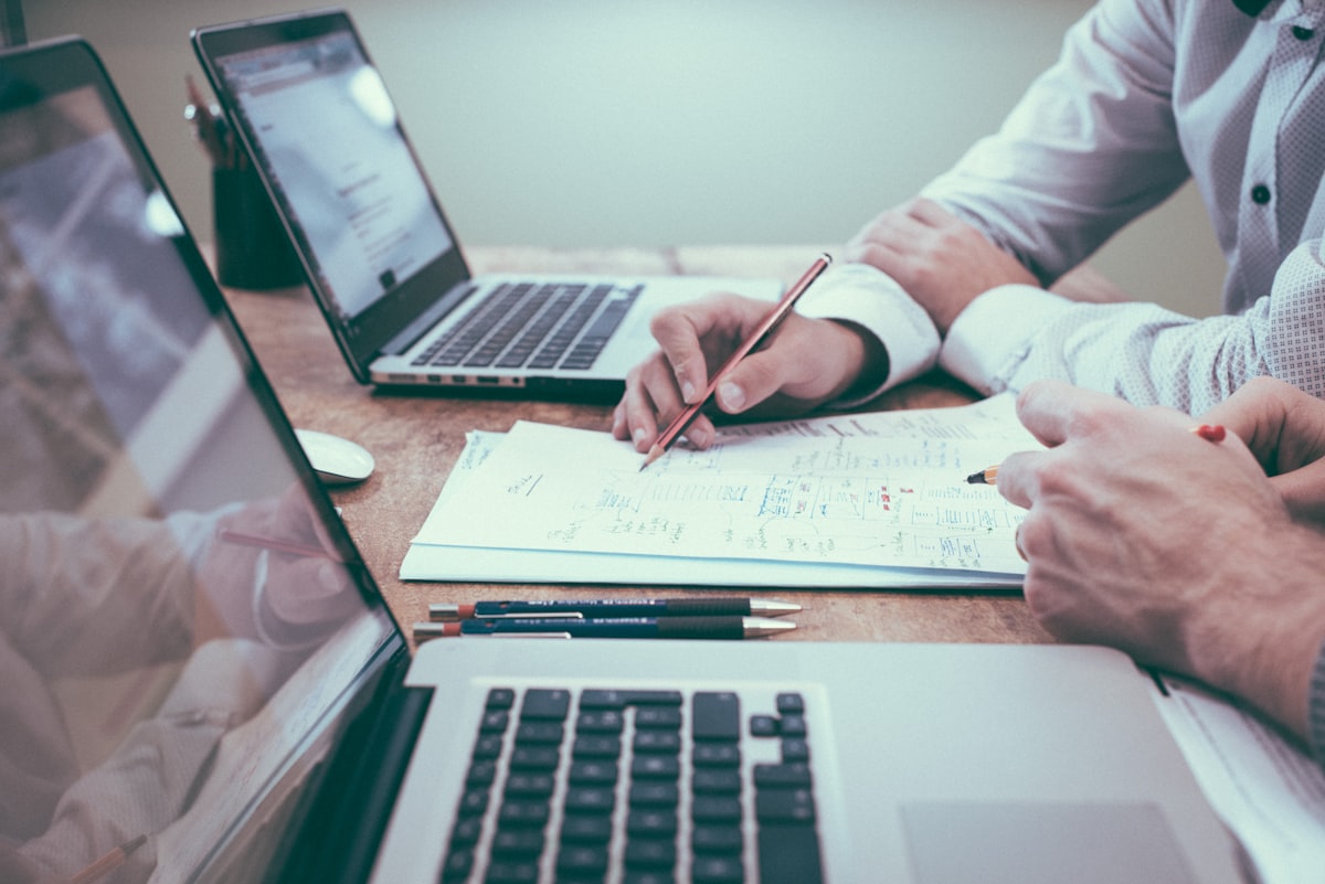 Deux professionnels analysant un document annoté sur un bureau, ordinateurs portables ouverts